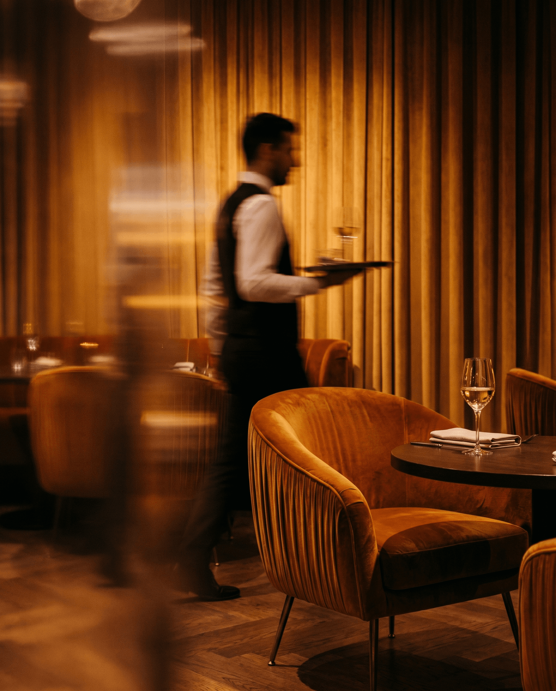 A waiter carrying drinks through a warmly lit restaurant