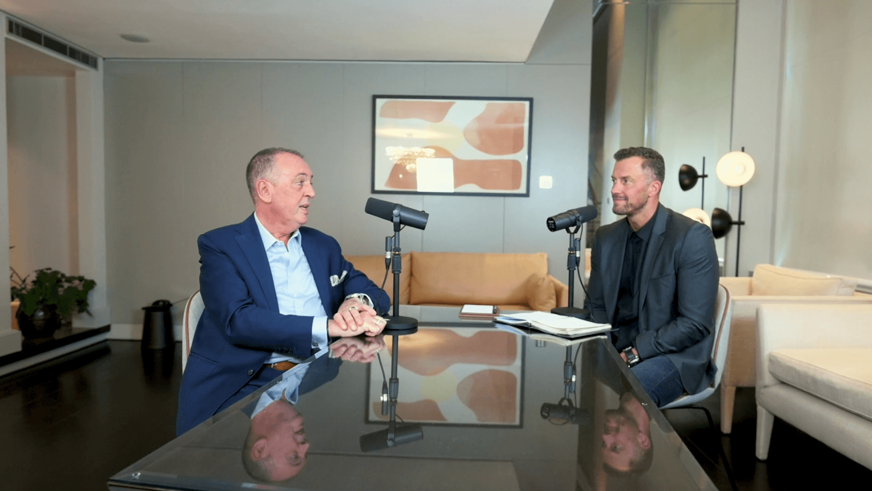 Two men in conversation across a desk with podcast microphones